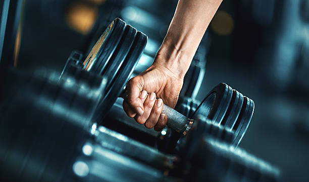 Closeup side view of unrecognizable person grabbing a dumbbell from a dumbbell rack. Shallow focus, toned image.