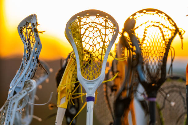 Girls women's lacrosse sticks in air at sunset